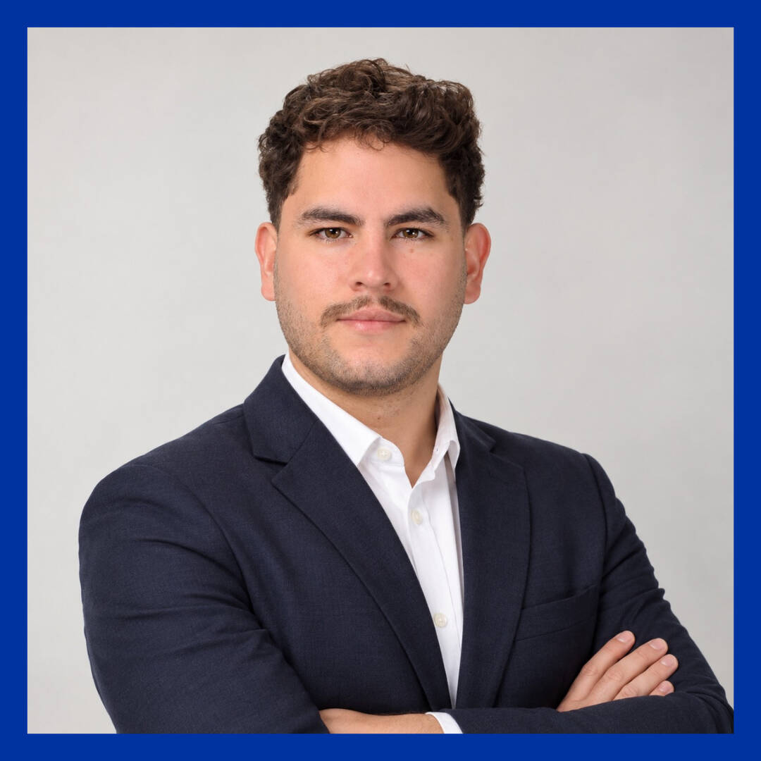 Pedro Pablo Quiros, PCE Outreach Graduate Assistant, in a navy blazer and white shirt with arms crossed, smiling slightly at the camera.